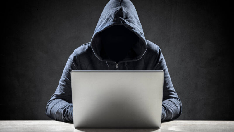 Concept of anonymous speech online with person in hooded sweatshirt with face not visible sitting at computer