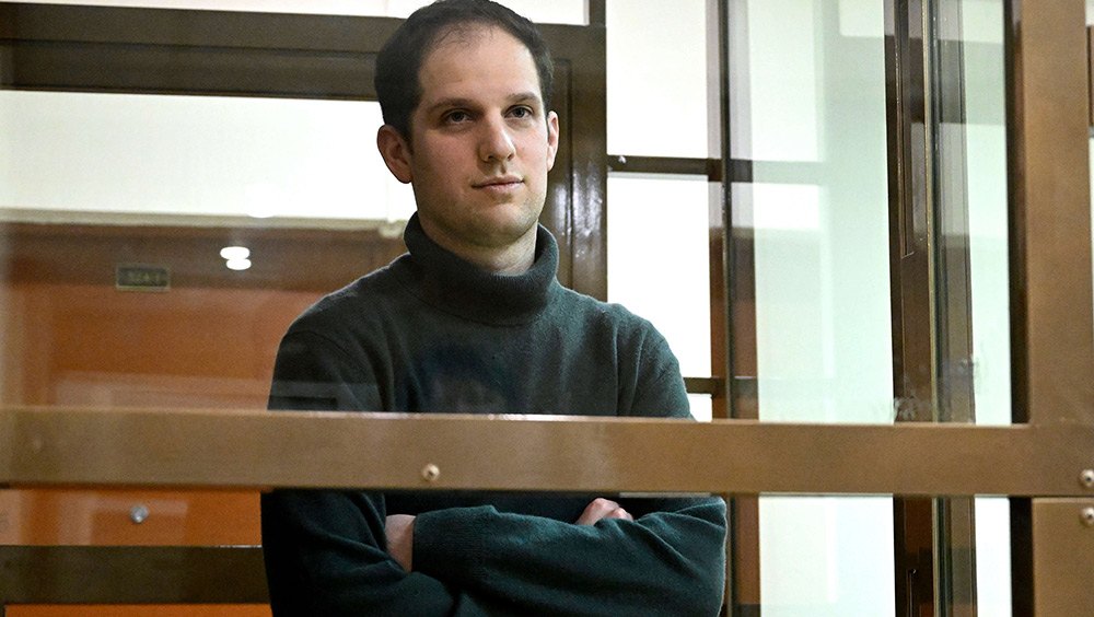 Wall Street Journal reporter Evan Gershkovich stands in a glass cage in a courtroom.