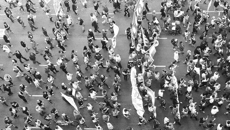 An aerial view of a group of protesters marching down a street holding signs, in black and white