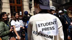 Photo of Columbia University journalism student with sign on back that reads Student Press Is Crucial