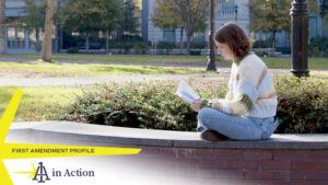 A photo showing Kate Lindley sitting on a brick wall outside reading a book, with text overlay reading First Amendment Profile: 1A in Action