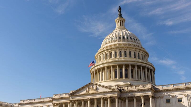 A view of the dome and front of the U.S. Capitol building against a blue sky, with the American flag flying out front