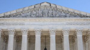 A closeup view of the front, upper portion of the Supreme Court building against a clear blue sky