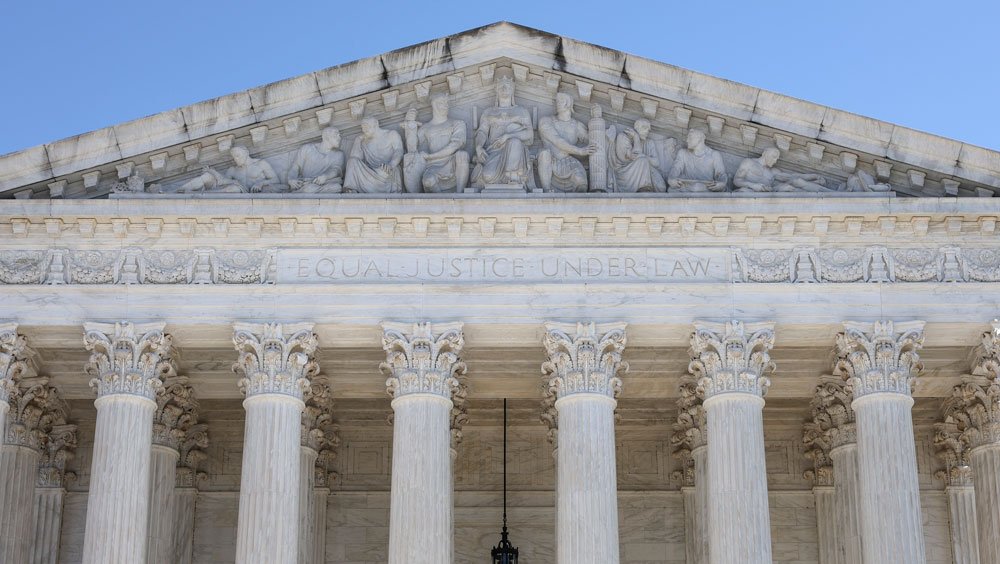 A closeup view of the front, upper portion of the Supreme Court building against a clear blue sky