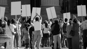 A black and white image showing the rear view of a group holding signs in protest