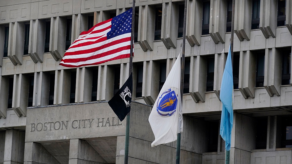 The American flag, the Commonwealth of Massachusetts flag, and the City of Boston flag, from left, fly outside Boston City Hall.