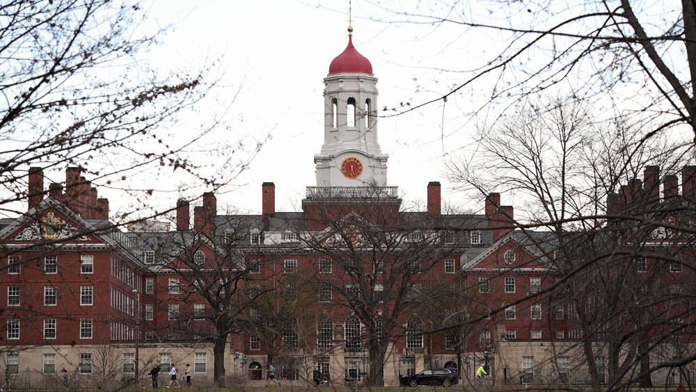 View of an old building on the Harvard campus, with bare trees in the foreground on a bright-white day
