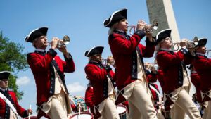 A group of parade participants wearing Revolutionary War-era bright red jackets and hats and playing brass instruments