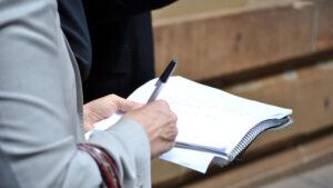 A close-up image showing a person holding a notebook with a pen poised to write