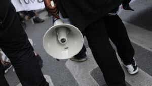 An image of a person's hand holding a megaphone as they stand on a crowded street
