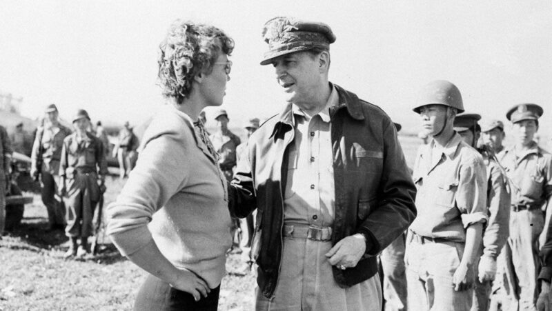 A historical black and white image of a woman speaking with a general, with soldiers in the background