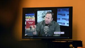 A view of a TV screen showing Alex Jones speaking, with the Infowars logo in the background