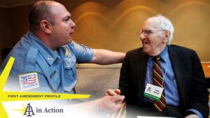 Frank Kameny, wearing a suit and tie, sits as he speaks with a man in a blue shirt. Text overlays the photo, reading "1A in Action: First Amendment profile"