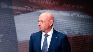 An image of Mark Kelly wearing a blue suit against a backdrop of the U.S. flag with text overlaying it.