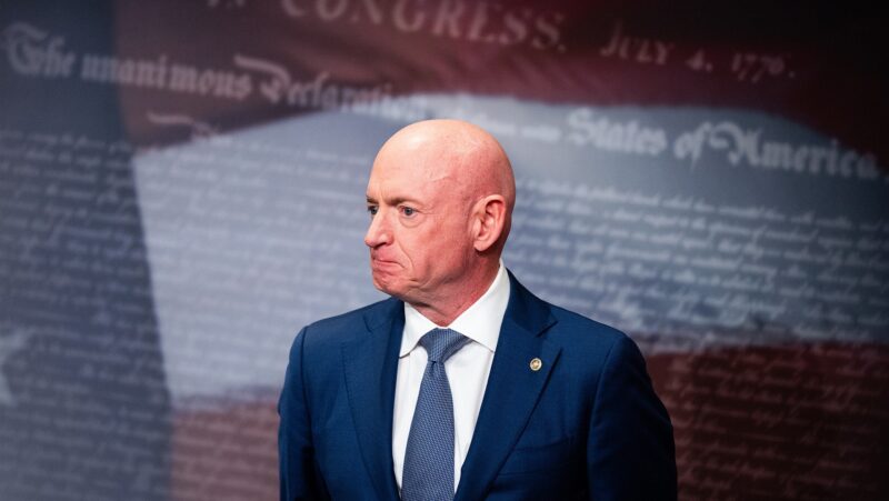 An image of Mark Kelly wearing a blue suit against a backdrop of the U.S. flag with text overlaying it.
