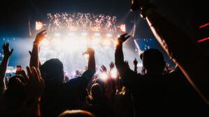 Audience members raise their hands in celebration as they face a well-lit stage
