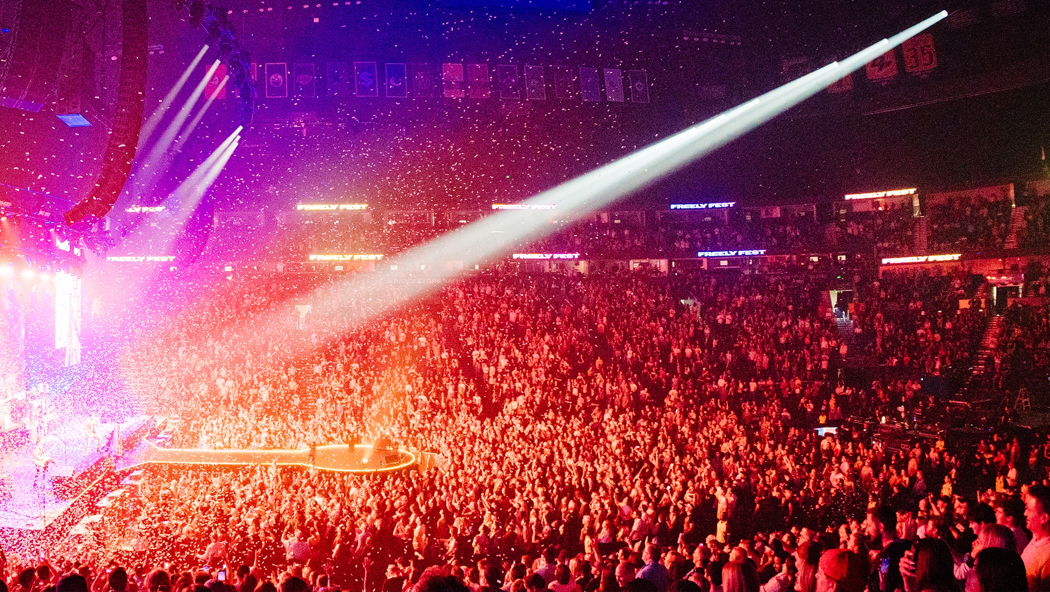 A crowd packs an arena, with red, orange and purple lighting throughout the space