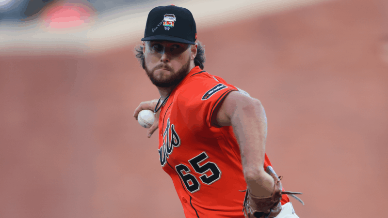 A baseball player wearing a bright-orange jersey prepares to throw a ball. He wears a hat with the rainbow version of the team logo, next to handwritten text that references a Genesis Bible verse.