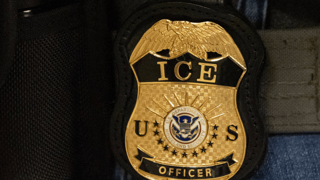 A gold badge on a black jacket, with the words "ICE U.S. OFFICER" inscribed on the badge