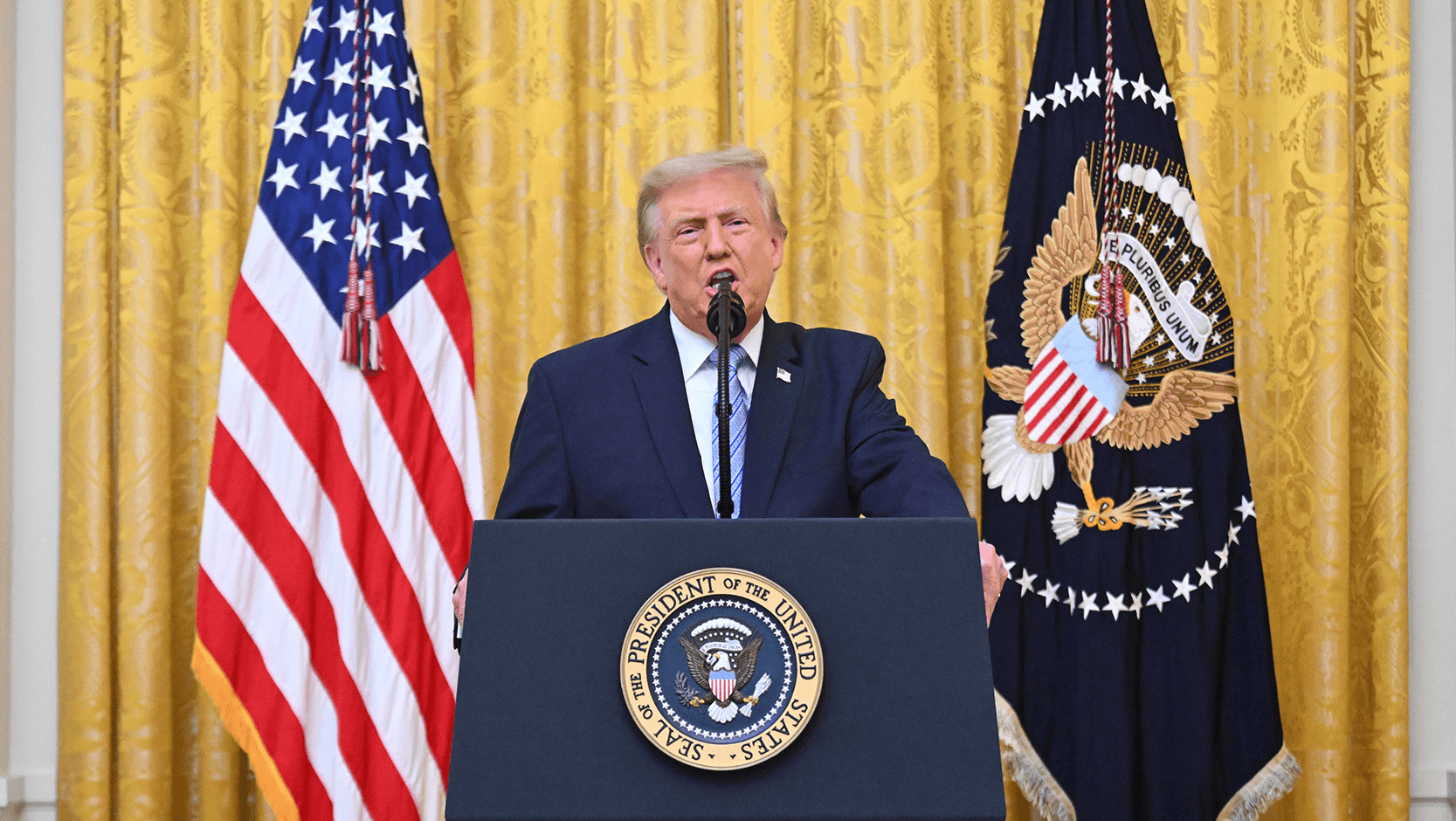 Donald Trump speaks as he stands behind a podium featuring the presidential seal